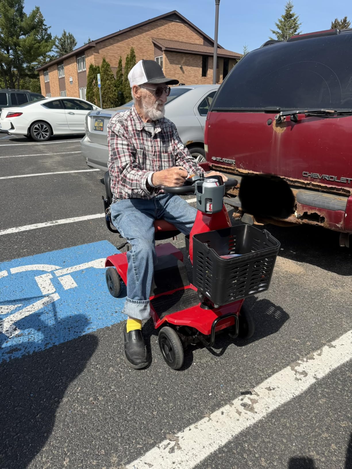 Customer riding the red mobility scooter with a full front basket in a parking lot